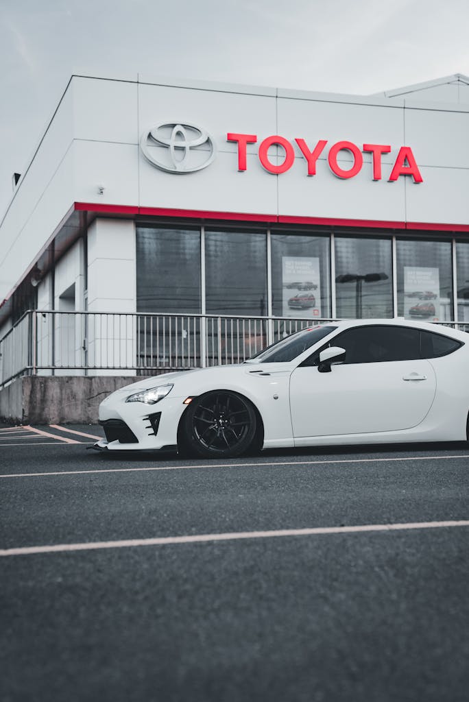 A sleek white car is parked outside a Toyota dealership on a cloudy day.