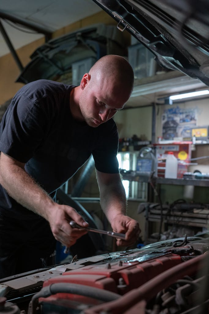 A mechanic is diligently working inside a garage, fixing a car engine under the hood.