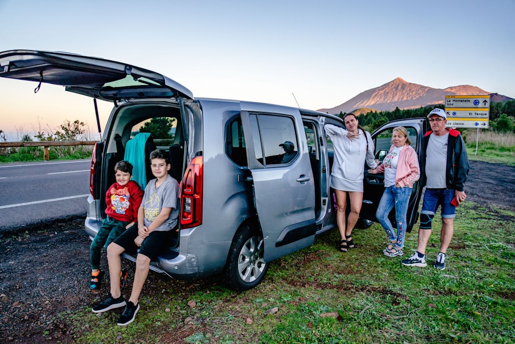 A family enjoys a scenic road trip by Mount Teide, Spain, with a van parked by the roadside.
