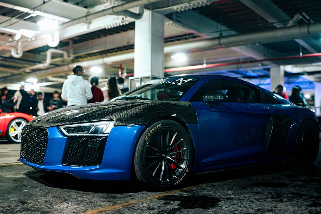 Sleek blue supercar with carbon fiber detailing at a car meet in a dimly lit garage.