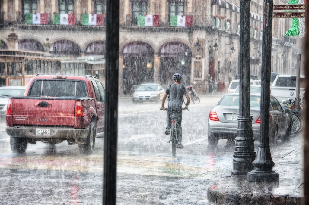 A cyclist rides through heavy rain in Morelia's urban street scene, Mexico.