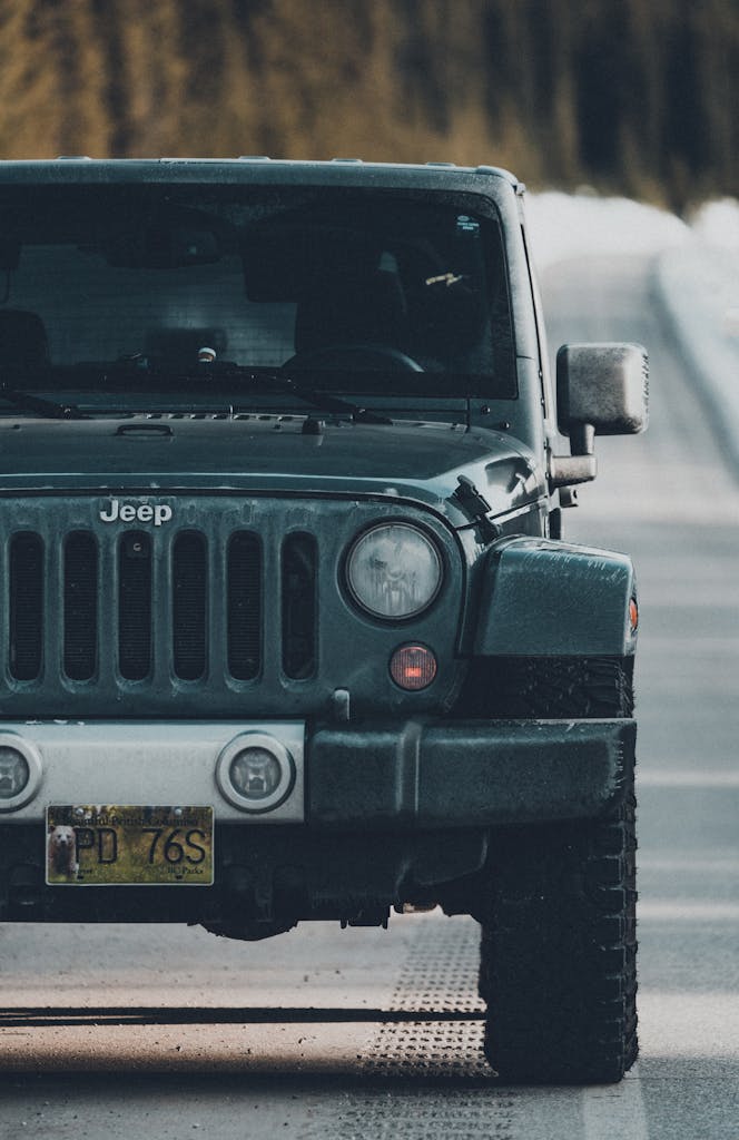 A rugged Jeep Wrangler travels down a dusty road, surrounded by nature.
