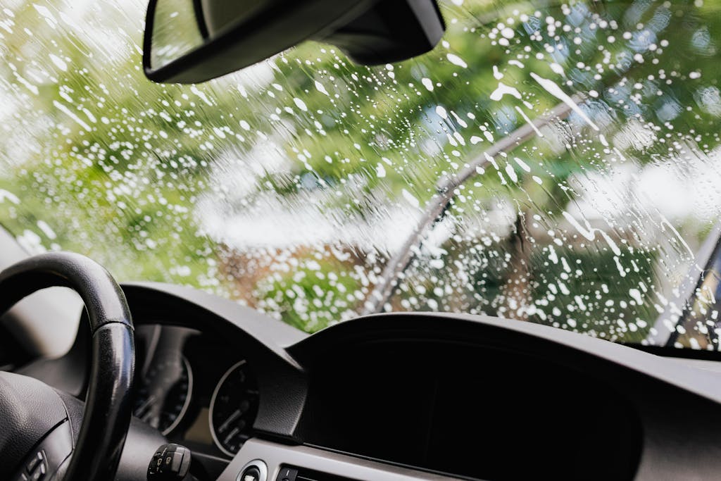 Imagen actual: Interior view of a car with soapy windshield during cleaning. Clear dashboard visible.