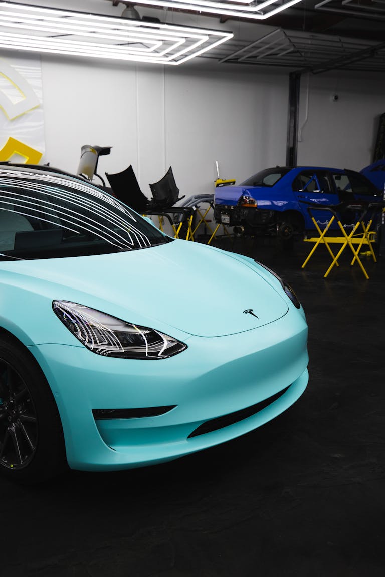 Modern turquoise Tesla car parked in a garage with overhead lights.