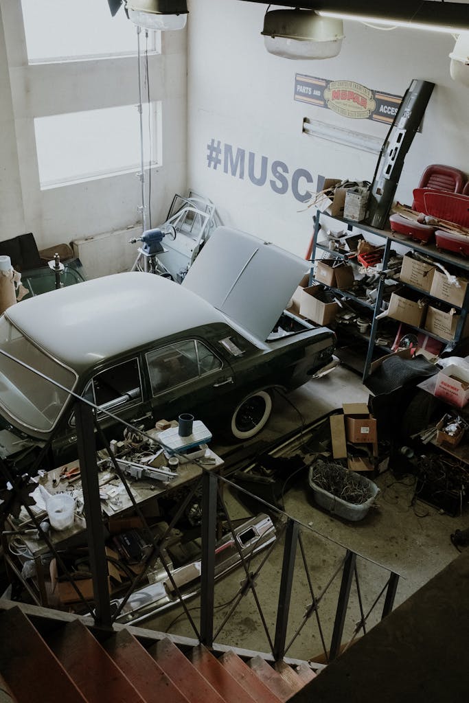 Imagen actual: A vintage car is being repaired in a cluttered automotive workshop with tools and equipment.