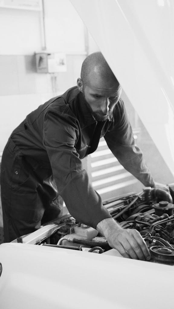 Male mechanic working under a car hood in a workshop, focusing on engine repair.
