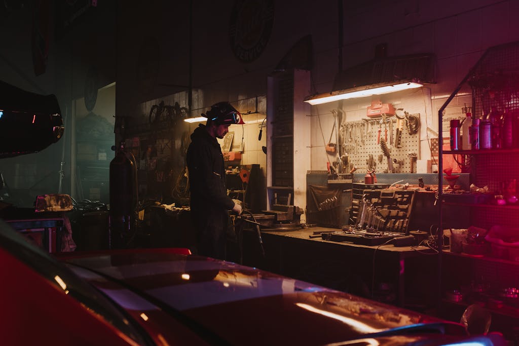 Imagen actual: Mechanic working in a dimly lit garage workshop surrounded by tools and equipment.