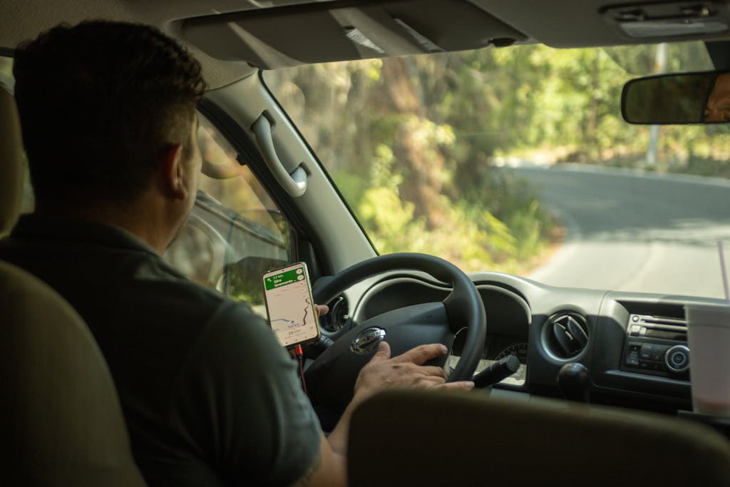 Imagen actual: Driver using a smartphone GPS app for navigation while on a curvy road surrounded by nature.