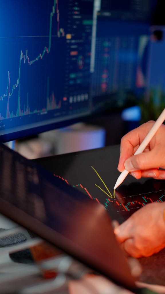 Imagen actual: Person using a stylus on a tablet for stock market analysis, with charts on a monitor.