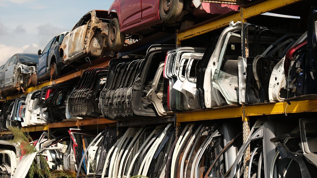Imagen actual: Rows of car doors stacked in a junkyard under a clear sky.