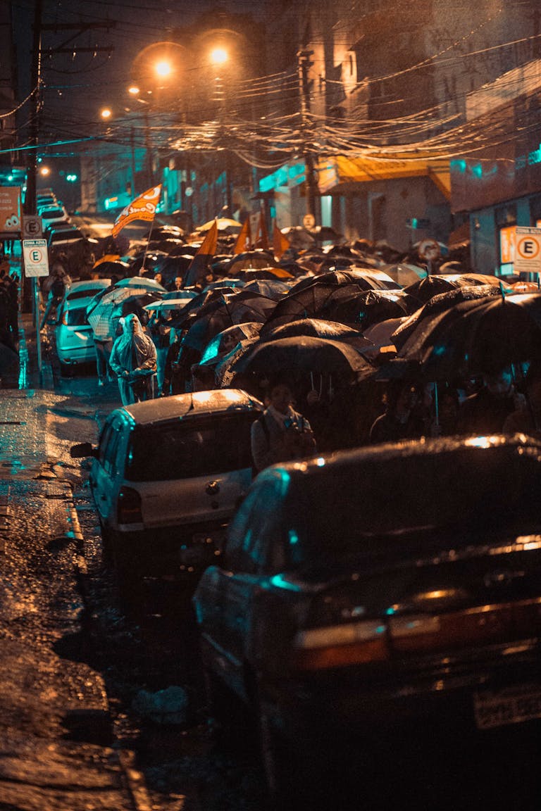 A vibrant urban street scene with cars and people under umbrellas in the heavy rain.