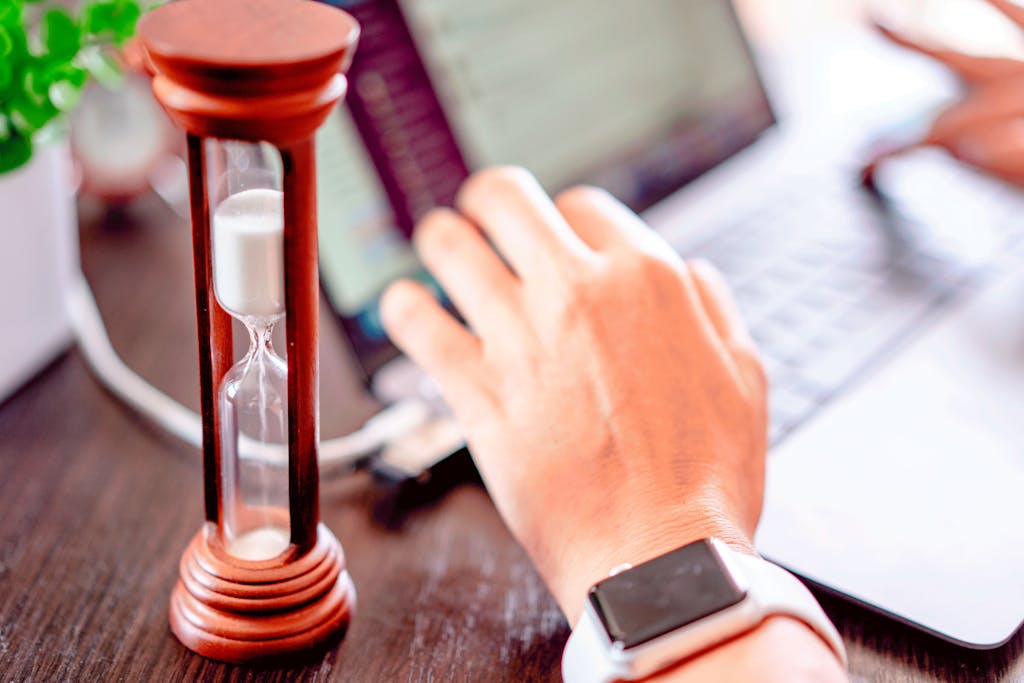 Imagen actual: Close-up of a hand on a laptop with an hourglass, symbolizing time management and productivity.
