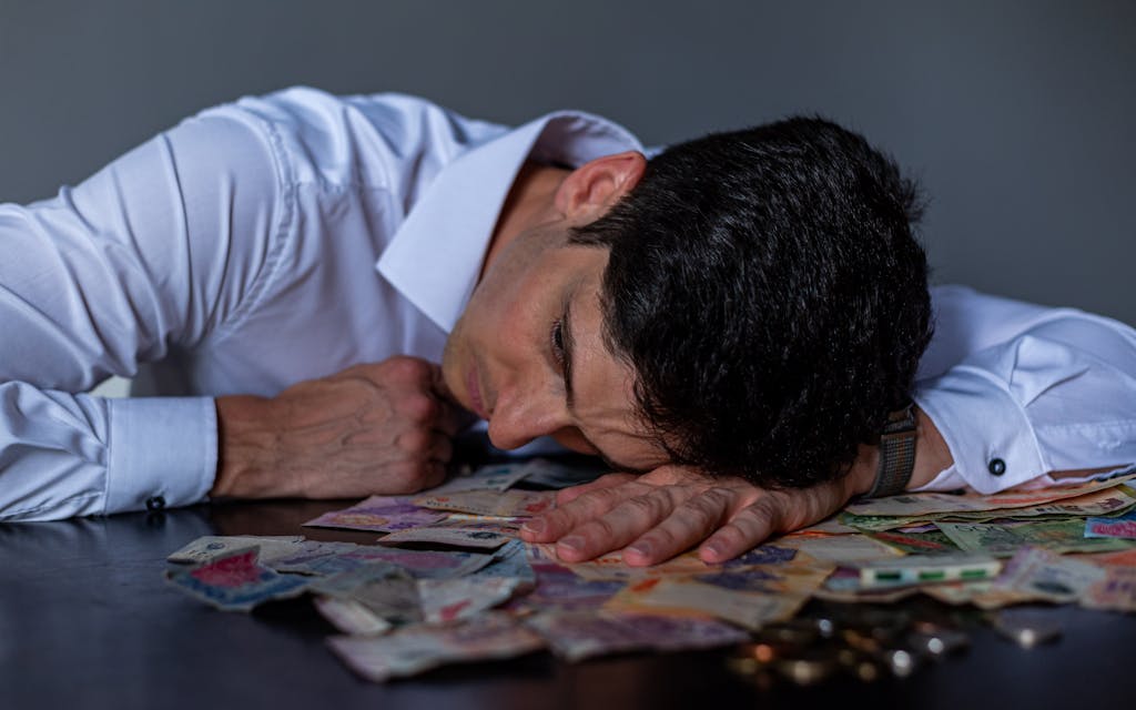 Imagen actual: Man in stress resting on table covered with Argentine pesos symbolizing financial hardship.