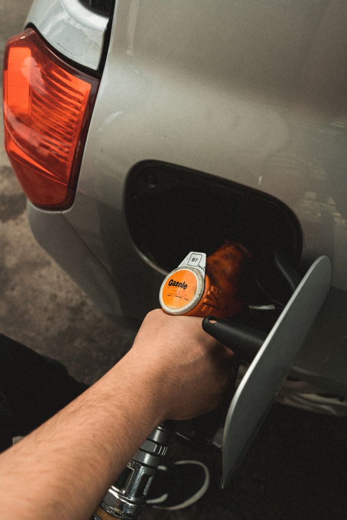 Imagen actual: Close-up of a hand refilling a car at a gas station during daylight.