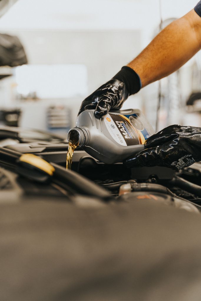Imagen actual: Close-up of a mechanic pouring engine oil into a car engine with gloved hands, indoors.